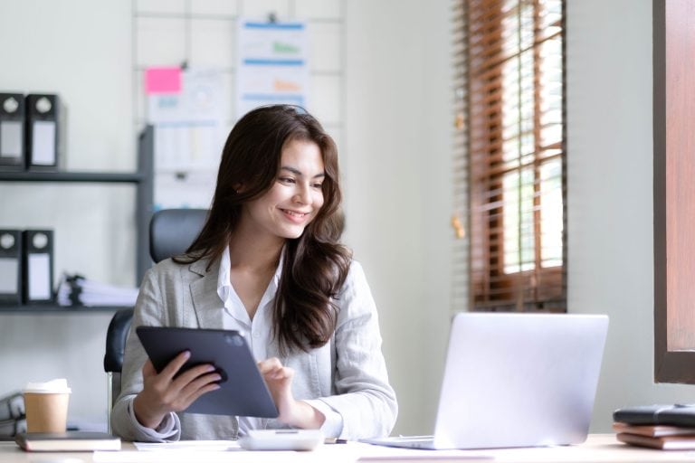 Femme souriante travaillant avec tablette et ordinateur portable.