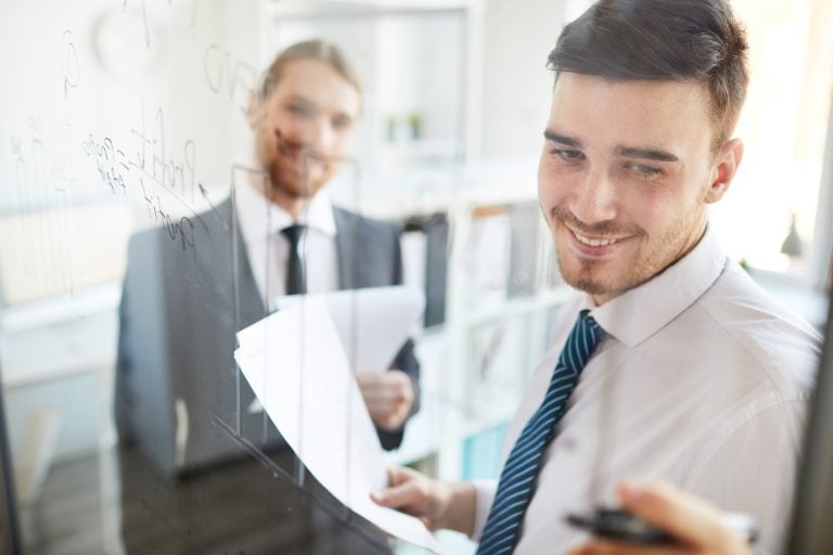 Homme souriant écrivant sur un tableau transparent.