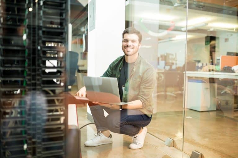 Homme souriant avec ordinateur portable dans bureau moderne.
