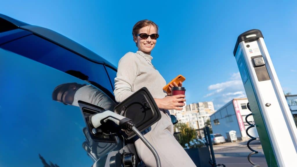Femme chargeant une voiture électrique avec café.